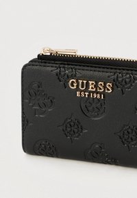 Crni kožni novčanik s utisnutim uzorcima logotipa, hardverom zlatne boje i zatvaračem na patentni zatvarač. Kompaktan pravokutni oblik s teksturiranom površinom.