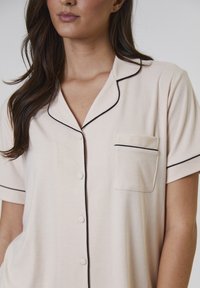 Jasnobeżowa piżama z krótkim rękawem, z kołnierzykiem typu notch, czarnym wykończeniem, przednią kieszonką i zapięciem na guziki. Teksturowana, prążkowana tkanina.