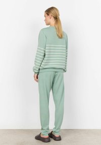 Sweatshirt vert menthe avec des rayures horizontales blanches, assorti à un jogging vert menthe et à des chaussures foncées. Matière douce, coupe décontractée.
