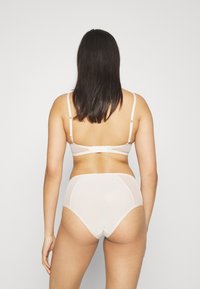 Beige lingerie set featuring a sheer back bra with adjustable straps and a matching high-waisted brief, both made from a smooth, lightweight fabric.