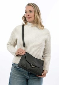 Borsa a tracolla in pelle grigia scura, con pattina arrotondata, hardware metallico e tracolla regolabile, tenuta da un modello in un maglione lavorato a maglia.