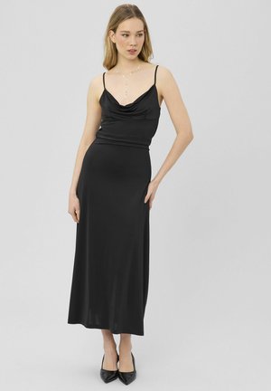 Robe noire, élégante et satinée, avec un col bénitier, des bretelles spaghetti ajustables et une silhouette droite, associée à des escarpins noirs pointus.