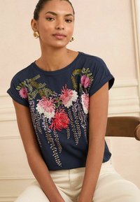 T-shirt a maniche corte di colore blu navy con ricami floreali colorati che ritraggono fiori rosa, rossi e viola. Tessuto morbido con vestibilità comoda.