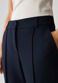 Marineblauwe op maat gemaakte broek met een gladde textuur, voorzien van een vlakke voorkant, zijzakken en een licht taps toelopend model.