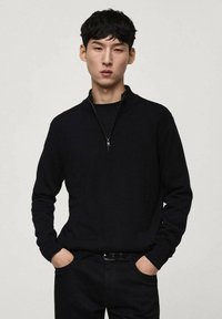Zwart sweatshirt met rits en lange mouwen, gemaakt van zacht materiaal. Ontspannen pasvorm, gecombineerd met zwarte broeken. Eenvoudig, minimalistisch ontwerp.