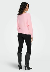 Suéter de punto rosa claro con ajuste holgado, combinado con jeans ajustados negros y botas negras de tacón hasta la rodilla.