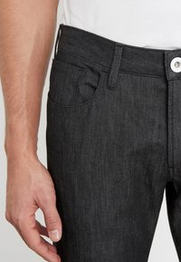 Černé džíny z denimu s vypasovaným střihem, rovný střih a přední kapsy. Textura látky je hladká s jemným leskem a robustním kováním.