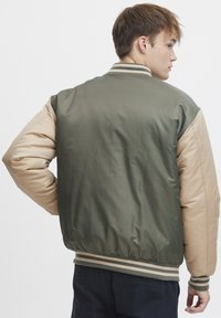 Giacca bomber verde e beige con polsini e vita elasticizzati, caratterizzata da una texture morbida e dettagli a righe. Vista posteriore mostrata.