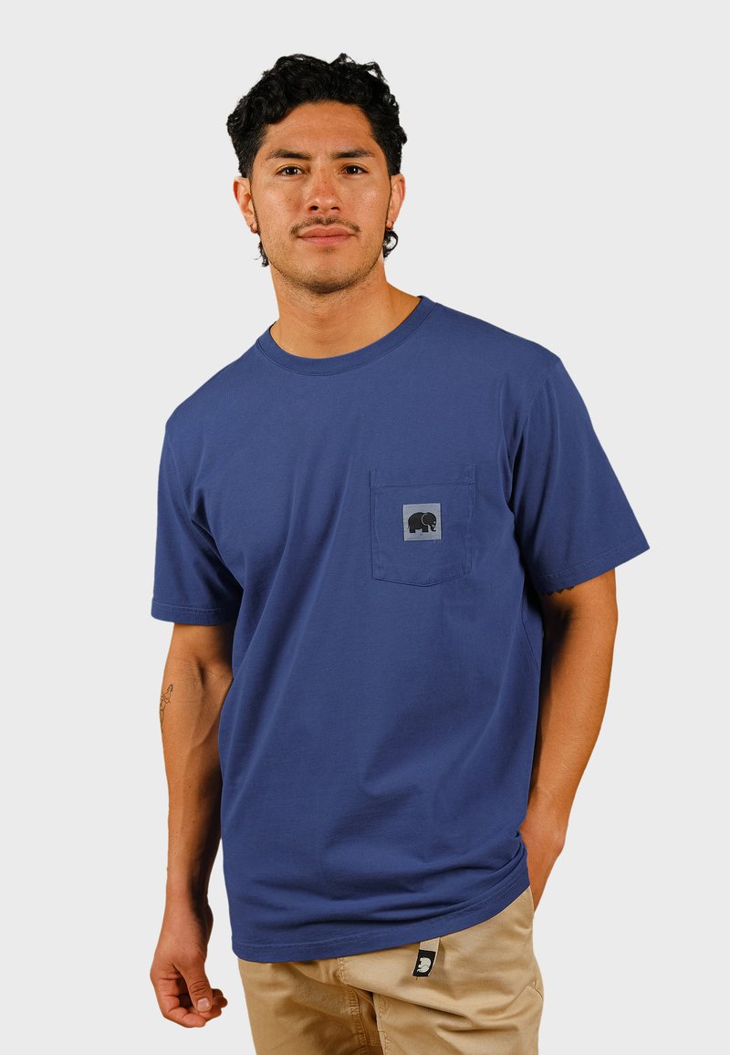 Blå bomulls T-shirt med korta ärmar, med en framficka och en grå elefantlogotyp på fickan. Tagg synlig vid nederkanten.