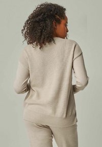 Hellbeige Pullover mit strukturiertem Strickfinish, der überschnittene Schultern und gerippte Bündchen hat. Die weiche, lockere Passform betont den Komfort.