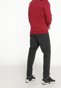 Sudadera roja con cuello redondo y logotipo en el hombro, combinada con pantalones ajustados gris oscuro y zapatillas negras. Textura suave, ajuste relajado.