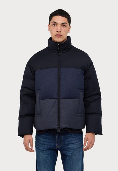 Puffer jacket with a high collar, dark navy upper and contrasting denim panel. Features a zip front and two side pockets.
