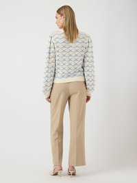 Pull en tricot à base crème, présentant un motif ondulé bleu et beige ; associé à un pantalon droit beige clair et des sandales à talons.