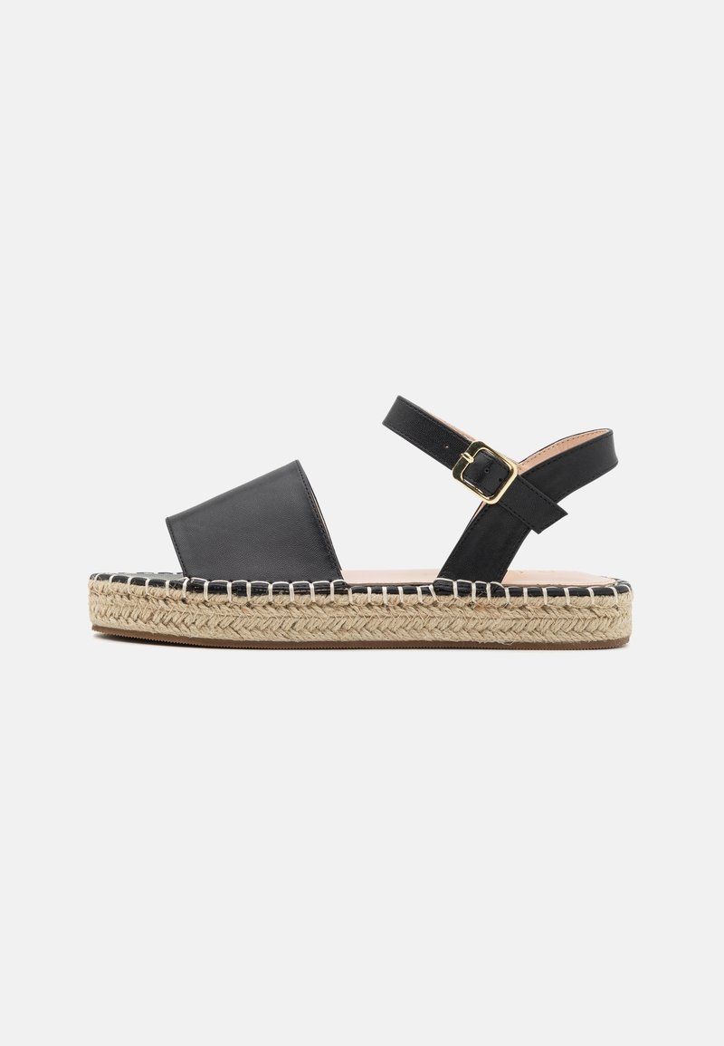 Sandale en cuir noir avec bride autour de la cheville, bout carré et plateforme en jute. Caractérisée par des coutures le long du bord et une boucle couleur dorée.