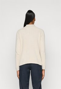 Un pull en tricot texturé beige clair avec un col montant et des manches longues, offrant une coupe décontractée et un ourlet légèrement arrondi.