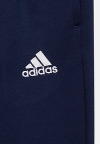Marineblå treningsbukser laget av et mykt stoff, med en hvit brodert "adidas"-logo og et enkelt, rent design.