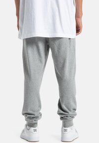 Graue Jogginghosen mit elastischen Bündchen und lockerer Passform, kombiniert mit weißen Turnschuhen, die ein Logo an der Ferse haben.