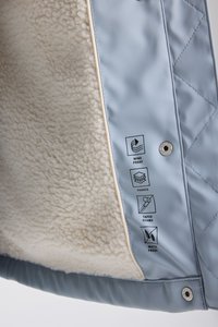 Vaaleansinine vuoritettu takki, jonka sisävuori on pehmeää kermaista materiaalia. Ominaisuuksiin kuuluu tuulenpitävyys, vedenpitävyys ja teipatut saumat, jotka näkyvät kankaassa ikonina.