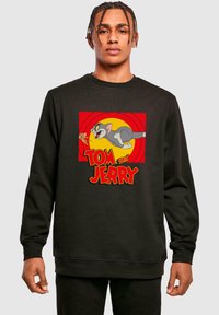 Fekete kapucnis pulóver, Tom és Jerry grafikával. A dizájn piros háttérrel, sárga körrel és alatta vastag betűkkel rendelkezik.