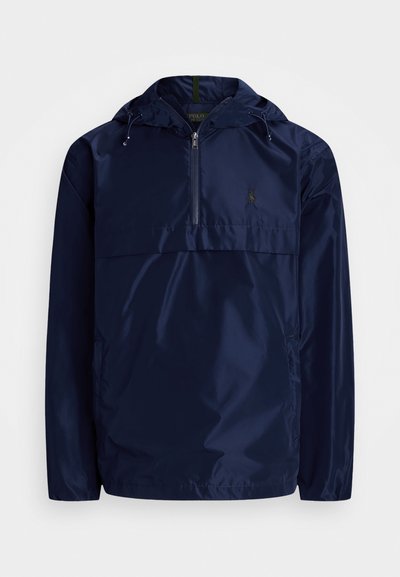 Veste pull bleu marine en tissu léger et brillant avec un zip avant 1/2, capuche réglable et poche avant. Détail discret du logo.
