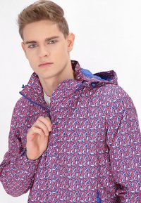 Jachetă cu model colorat, având un fermoar și glugă de culoare albastră. Designul include forme intercalate în nuanțe de roz și albastru.