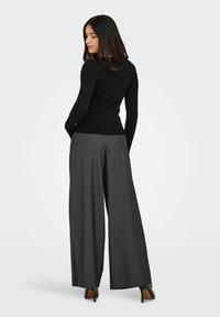 Črna rebrasta dolgosleeve majica v kombinaciji z visokim pasom sivimi širokimi hlačami s pinstripes vzorcem, ki imajo prilagojen kroj in eleganten design.