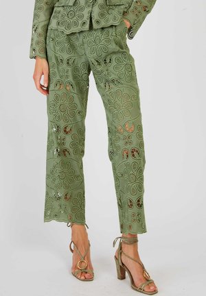 Koronkowe spodnie w kolorze oliwkowej zieleni z kwiatowymi wycięciami, zestawione z pasującą bluzką z długim rękawem oraz oliwkowymi sandałami na obcasie z paskami wokół kostki.