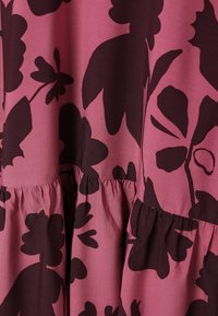 Blomstret kjole i lyserødt stof med mørk vinrød blomsterprint. Designet inkluderer et rynket lag ved kanten, der fremhæver tekstur og detaljer.