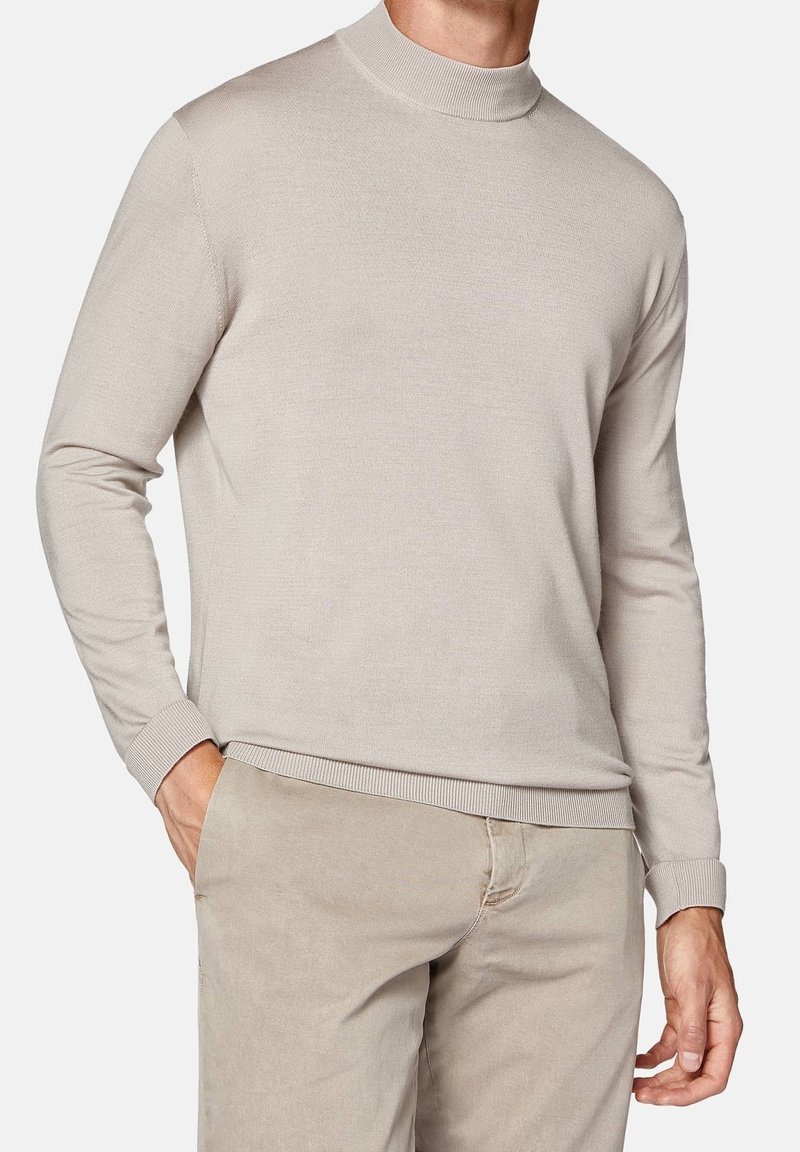 Pull beige à manches longues avec un col haut, des poignets et un ourlet côtelés, fabriqué en tissu tricoté lisse. Associé à un pantalon beige clair.