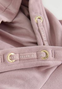 Light pink fabric with a soft texture featuring gold hardware eyelets and a stitched tag. Designed for adjustable fitting.