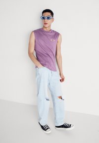 Purple sleeveless shirt with small logo, light blue ripped jeans, and black sneakers. Accessories include blue oval sunglasses.