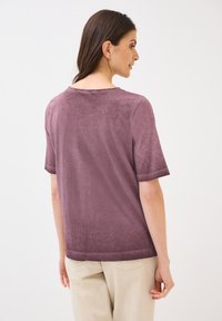 Kortærmet, mauve strikbluse med en afslappet pasform, der har en rund halsudskæring og subtil tekstur. Bagudsigten fremhæver det enkle design.