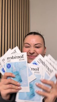 Eight facial mask packets featuring a blue design with water splash graphics. The packets are stacked in hands against a neutral background.