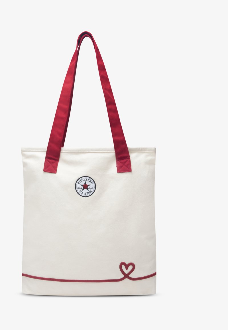 Τσάντα χειρός από καμβά, εκρού χρώμα με κόκκινες λαβές, με κυκλικό λογότυπο και κόκκινη διακοσμητική γραμμή σε σχήμα καρδιάς στο κάτω μέρος.
