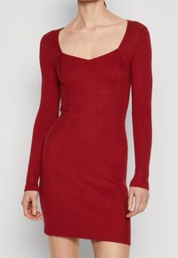 Czerwona sukienka z prążkowanej tkaniny, z długimi rękawami, dopasowanym krojem i kwadratowym dekoltem. Wykonana z elastycznego materiału, co zapewnia obcisłe dopasowanie.