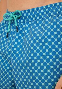 Modré plavky s vzorom a s nastaviteľným pásom, s geometrickým dizajnom v svetlomodrej a teal farbe. Hladká, ľahká tkanina.