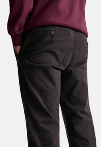 Les pantalons en coton noirs présentent une texture lisse, une taille ajustée avec des boutons décoratifs et des poches latérales. Le design inclut des lignes et des coutures subtiles.