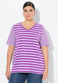 Camiseta de cuello en V a rayas moradas y blancas, con mangas cortas, hecha de una tela suave, de corte relajado, combinada con jeans azules.