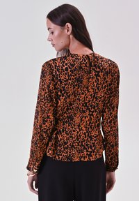 Blusa a maniche lunghe con stampa leopardata arancione e nera, caratterizzata da un'apertura a chiave nella parte posteriore e un tessuto testurizzato.
