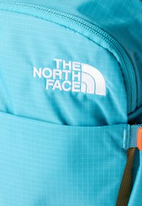 Ύφασμα σακιδίου πλάτης της The North Face σε ανοιχτό γαλάζιο χρώμα με λευκό κε ντημένο λογότυπο και ορατά ραφές κοντά σε φερμουάρ και πόρπη ιμάντα.