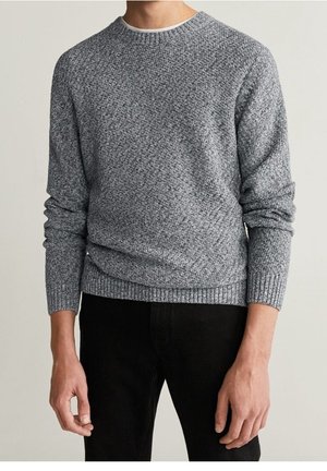 Hombre vistiendo un suéter ajustado de punto gris texturizado de manga larga con puños y dobladillo acanalados, combinado con pantalones negros.