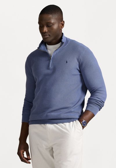 Lys blå strikket halv-zip sweater med ribbede manchetter og kant, prydet med et lille logo på brystet, sammen med hvide bukser.