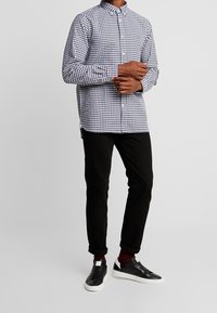 Chemise à boutons en motif vichy bleu et blanc, associée à un pantalon slim noir et des baskets noires avec semelles blanches.