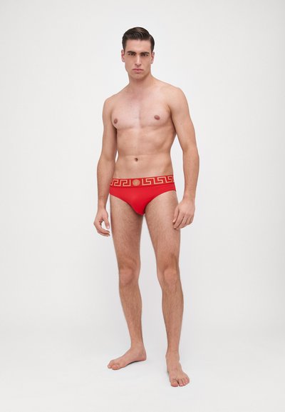Rote Badebrille mit einem goldenen griechischen Schlüsselmusterm entlang des Taillenbundes. Der Stoff wirkt glatt, mit einem enganliegenden Design und minimaler Abdeckung.