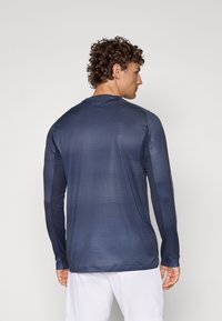 Maglietta atletica a maniche lunghe di colore blu navy, caratterizzata da un tessuto testurizzato e un design aderente, con pannelli laterali a contrasto e collo a giro.