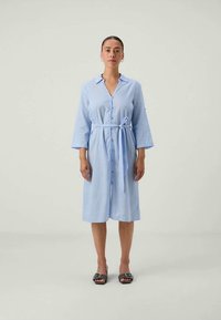 Vestido camisola listrado azul claro com fecho frontal de botões, mangas três quartos e cinto de tecido. Textura suave, design até ao joelho.