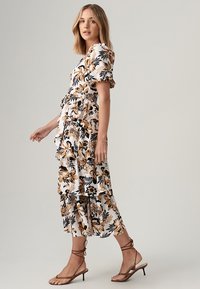Floral print maxi dress featuring white fabric with black and brown flowers, ruffle details, and short sleeves. Complemented with strappy sandals.