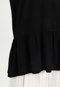Top in cotone nero con orlo arricciato, rifinito con una texture liscia. Il capo ha una vestibilità rilassata, un design semplice e senza hardware visibile.