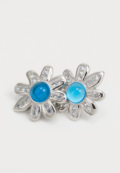 Orecchini floreali in argento con pietre circolari blu al centro, circondati da piccoli strass trasparenti. Design a forma di petalo con finitura lucida.