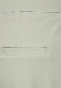 Ljusgrön tyg, slät yta, med en bakficka med en diskret sömnadsdetalj och en ren, minimalistisk design.